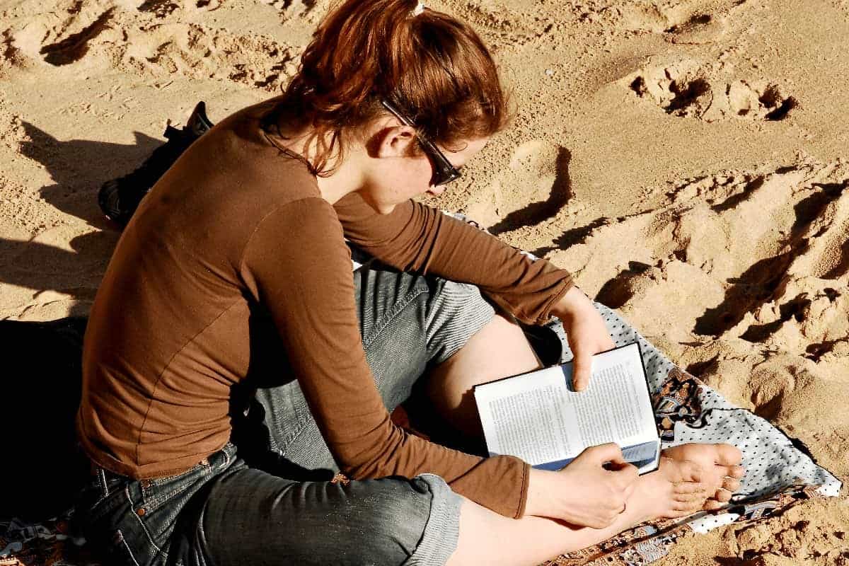 mujer joven sentada en la arena leyendo sobre turismo literario